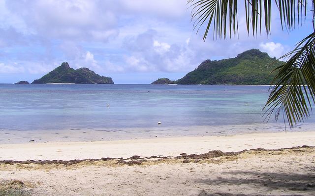 Zonnig uitzicht vanaf een strand met palmen over de Mamanuca-eilanden