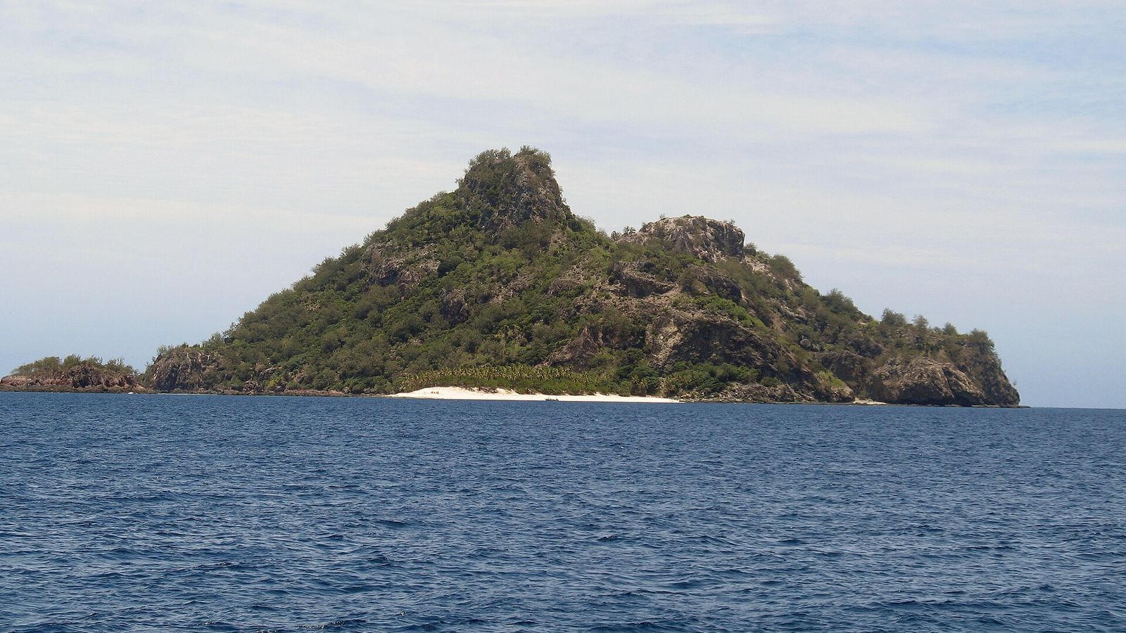 Monuriki vanaf zee gezien, met een begroeide rotspiek boven een smal strand