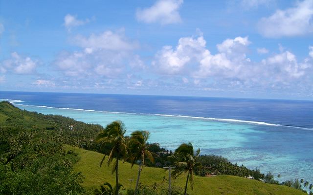 Uitzicht vanaf een heuvel over palmen en de turquoise lagune met het buitenrif van de Cookeilanden
