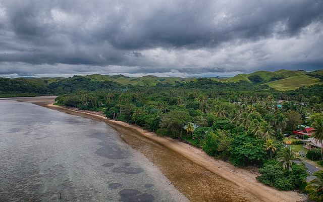 Kustlijn van de Coral Coast met een rif bij laagwater, palmen en groene heuvels