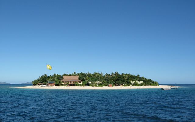 Het kleine Beachcomber Island met palmen, wit strand en een parasailer erboven