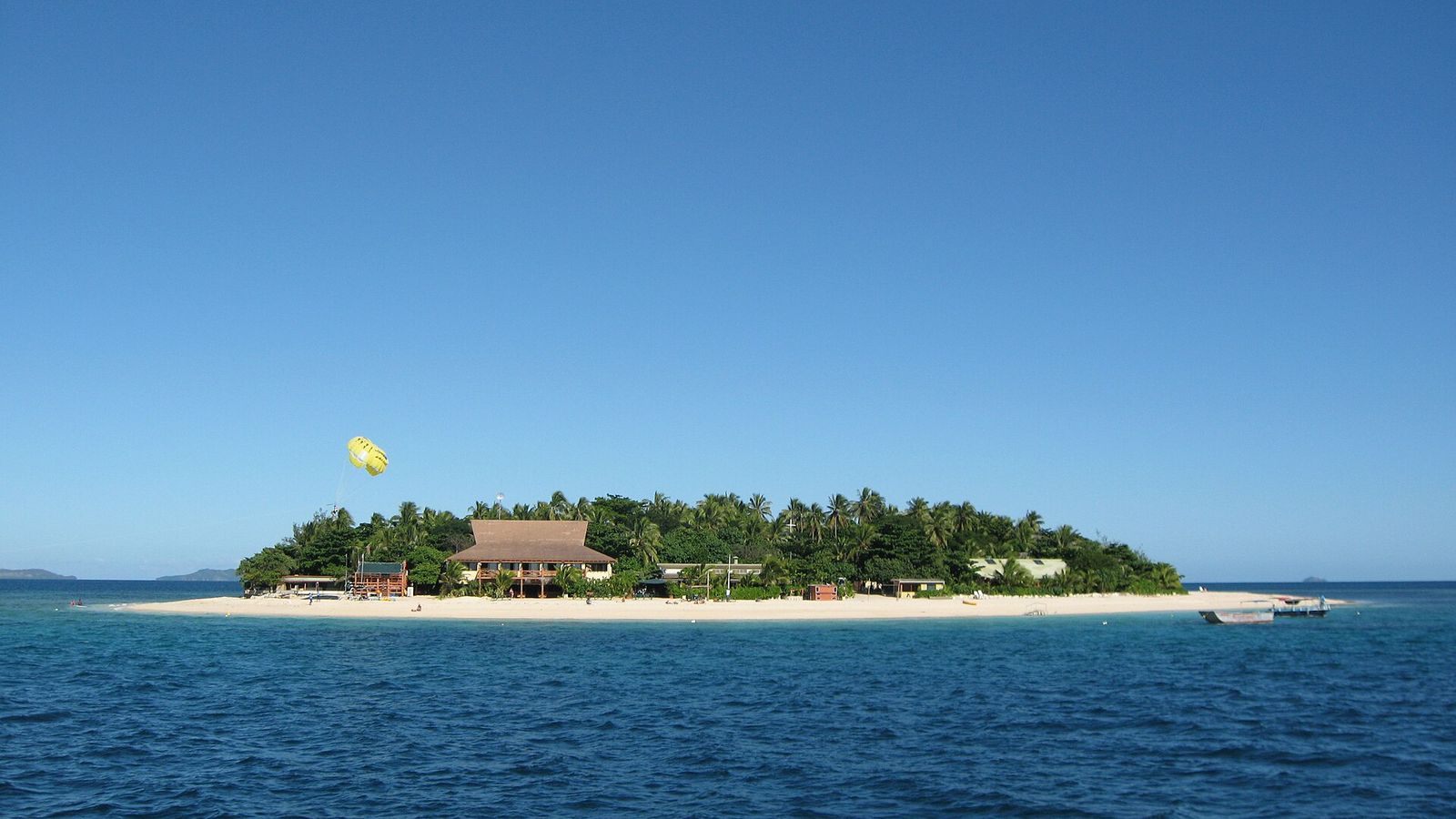 Het kleine Beachcomber Island met palmen, wit strand en een parasailer erboven