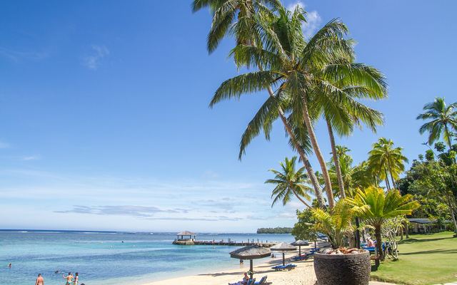 Strand met palmen, parasols en een steiger bij het Warwick Fiji Resort aan de Coral Coast