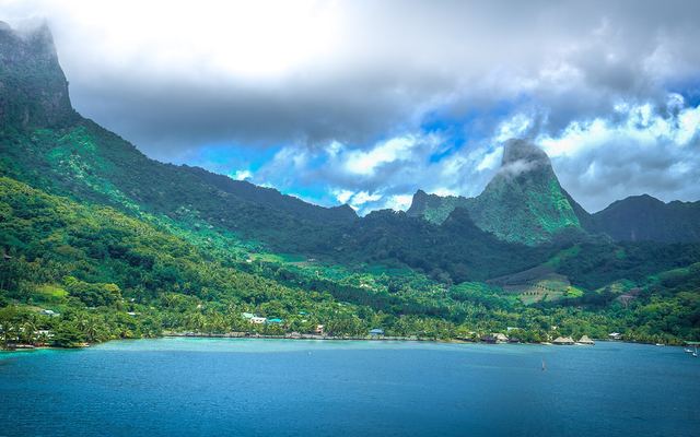 Groene, steile bergen en een diepblauwe baai met huisjes aan de kust in Frans-Polynesië